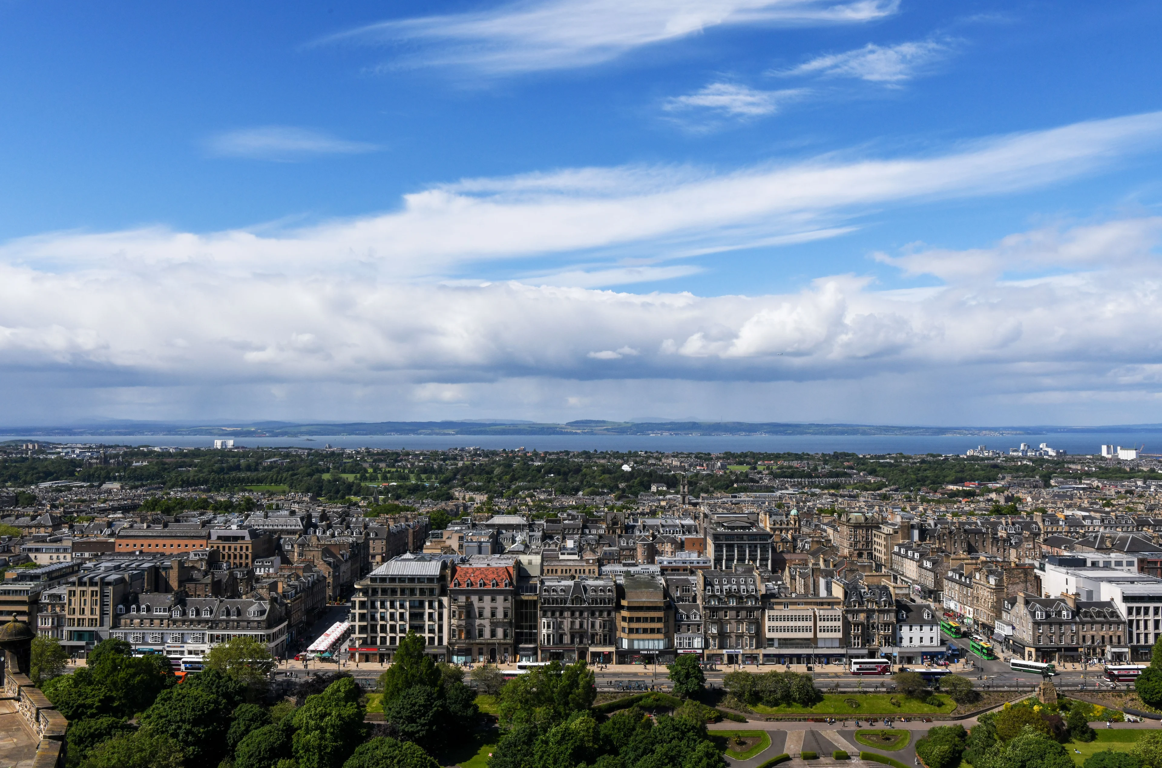 Panoramic view over Edinburgh rooftops toward the Firth of Forth on a sunny day